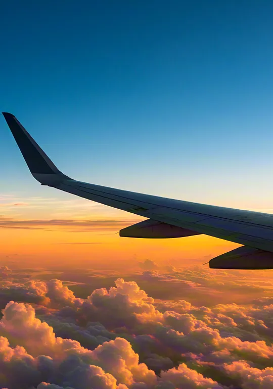 Airplane wing view above the clouds during sunset