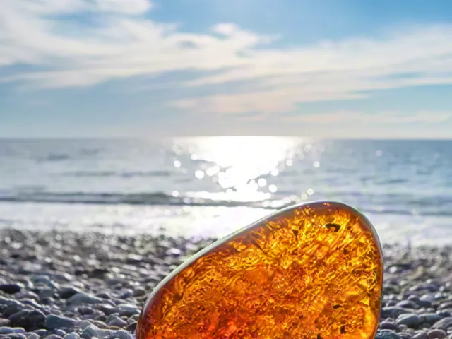 Amber gemstone glowing under sunlight on pebbles