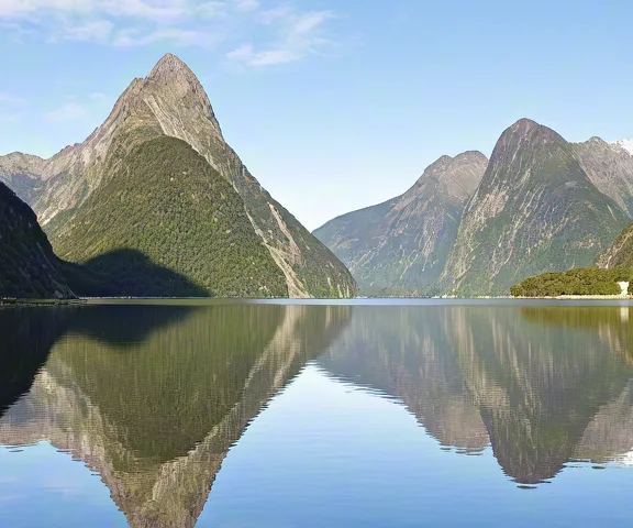 Calm blue water reflecting tall cliffs and bright sky in a mountain fjord.