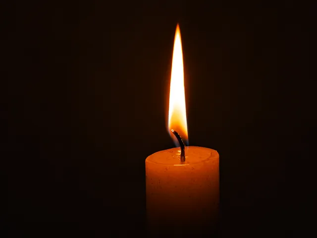 Single burning candle with a bright flame in a dark background, symbol of warmth and serenity