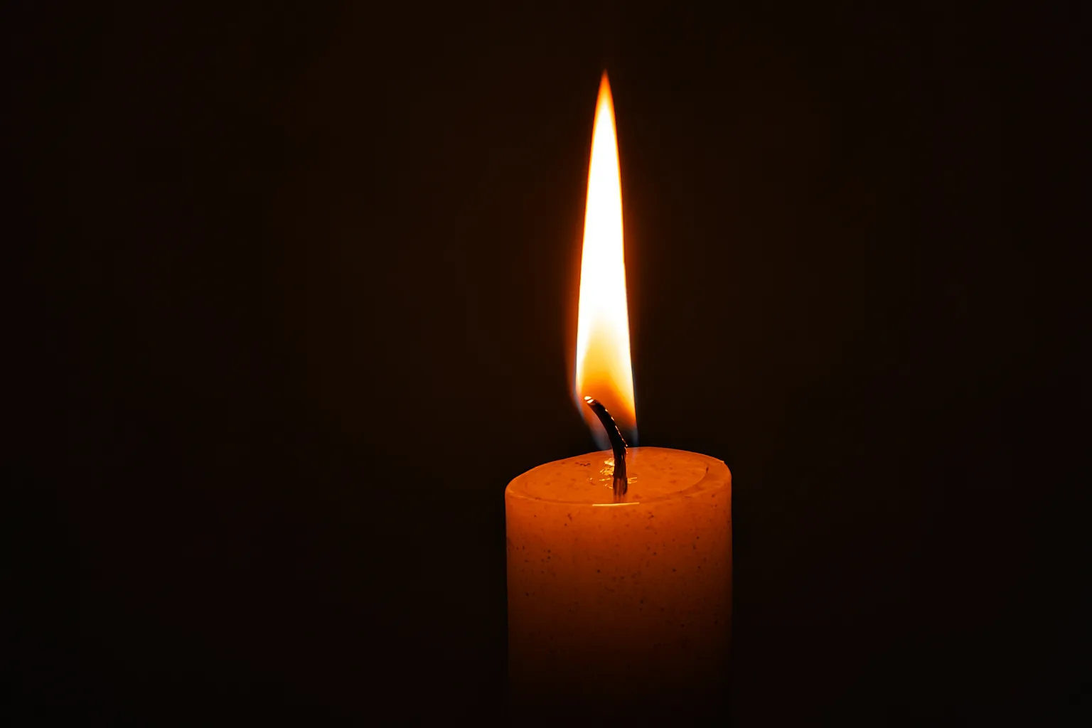 Single burning candle with a bright flame in a dark background, symbol of warmth and serenity