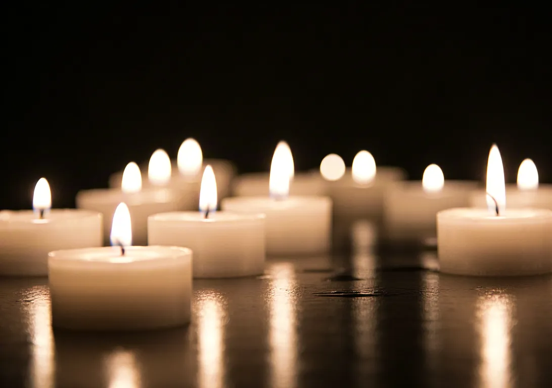 Row of small burning candles creating a peaceful, relaxing atmosphere on a dark reflective surface.