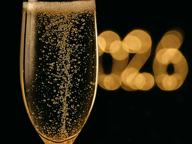 Close-up of a champagne glass with golden bubbles and blurred 2026 lights in the background