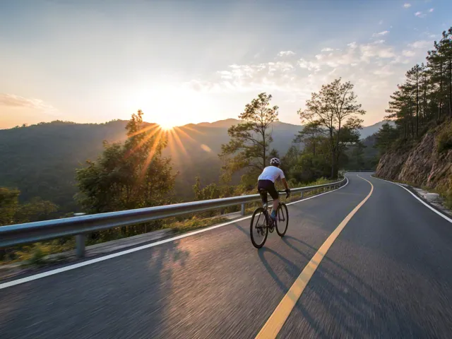 Man cycling on curving mountain road during sunrise