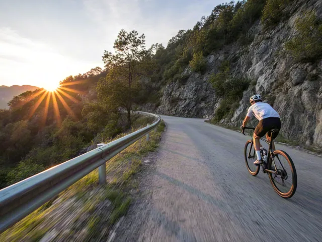Cyclist on curving road with sunset sky