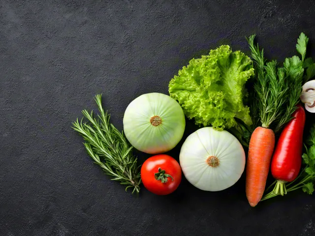 Assorted vegetables including tomatoes, carrots, and lettuce on black surface.