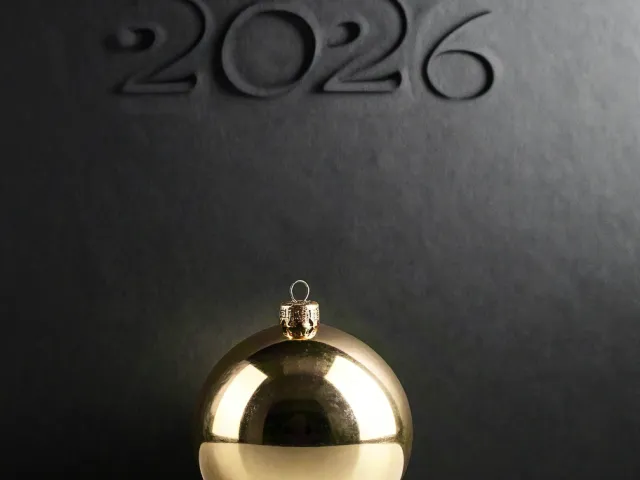 Golden Christmas ornament beside embossed 2026 text on black surface