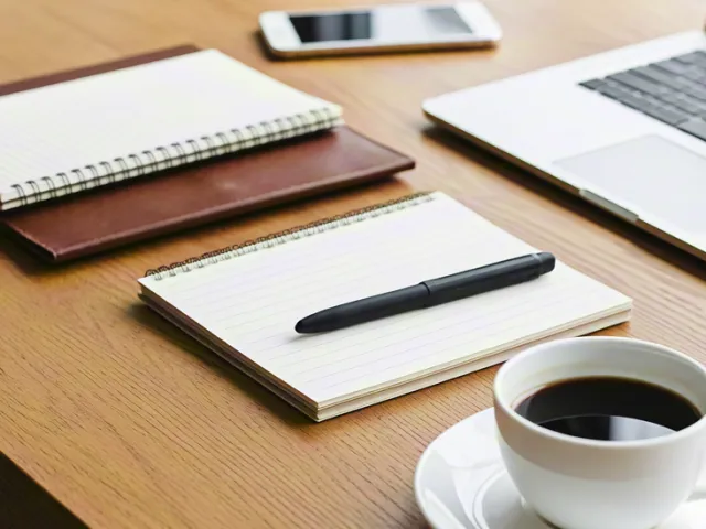office desk with notebook, laptop, and coffee cup