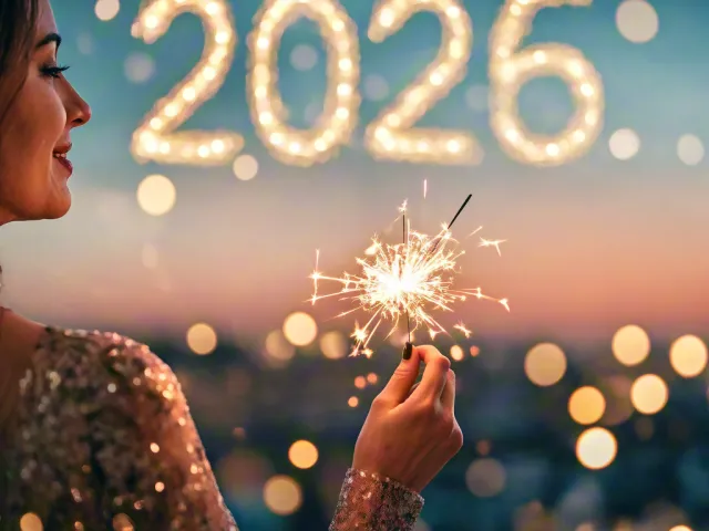 woman holding sparkler with blurred 2026 lights behind her