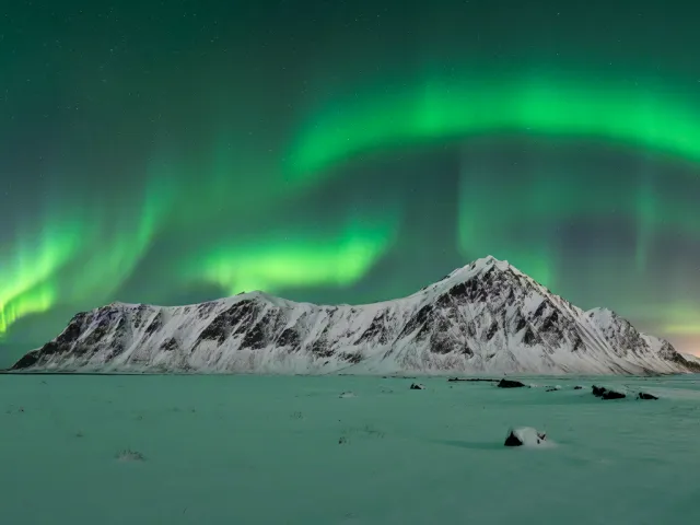 Bright green aurora above snowy mountain landscape