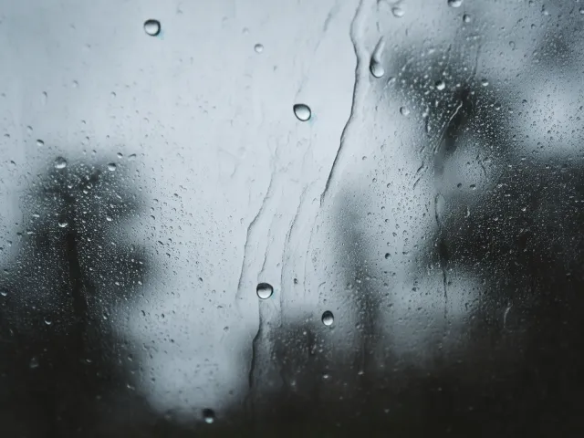 Water drops streaming on glass with misty background.