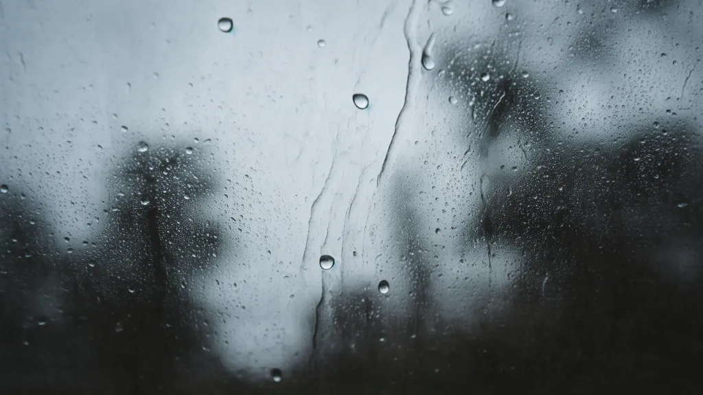 Raindrops on glass with gloomy sky reflection
