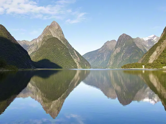 Tranquil fjord surrounded by steep mountain slopes reflected in clear water.