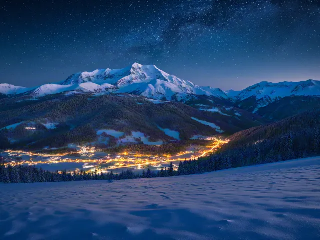 Winter town lights under snowy mountain range