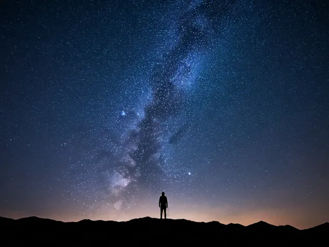 Milky Way night sky above person standing on hill