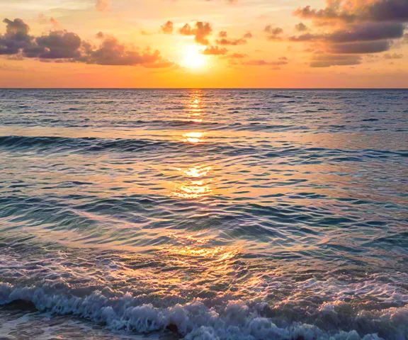 Evening sun setting over tranquil waves on sandy beach.