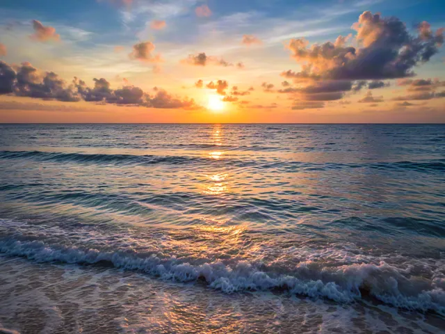 Golden sunset reflecting on gentle sea waves at beach shoreline.