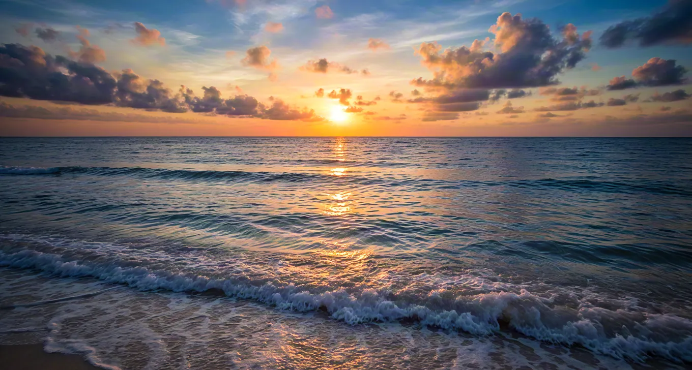 Golden sunset reflecting on gentle sea waves at beach shoreline.