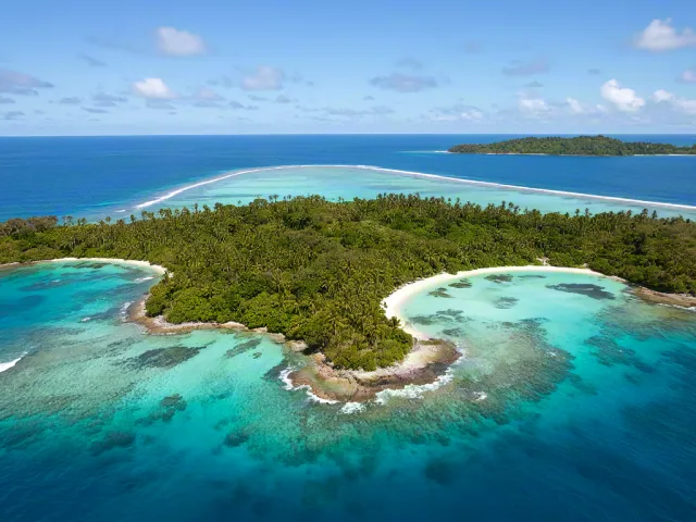 Drone view of small tropical island surrounded by bright turquoise sea